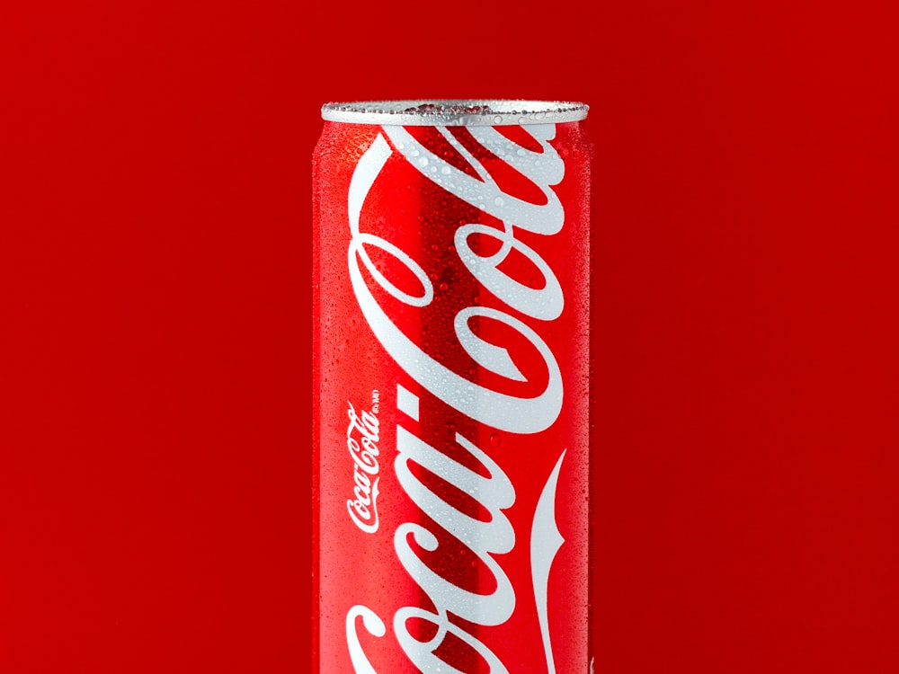 A chilled can of soda against a bright red background