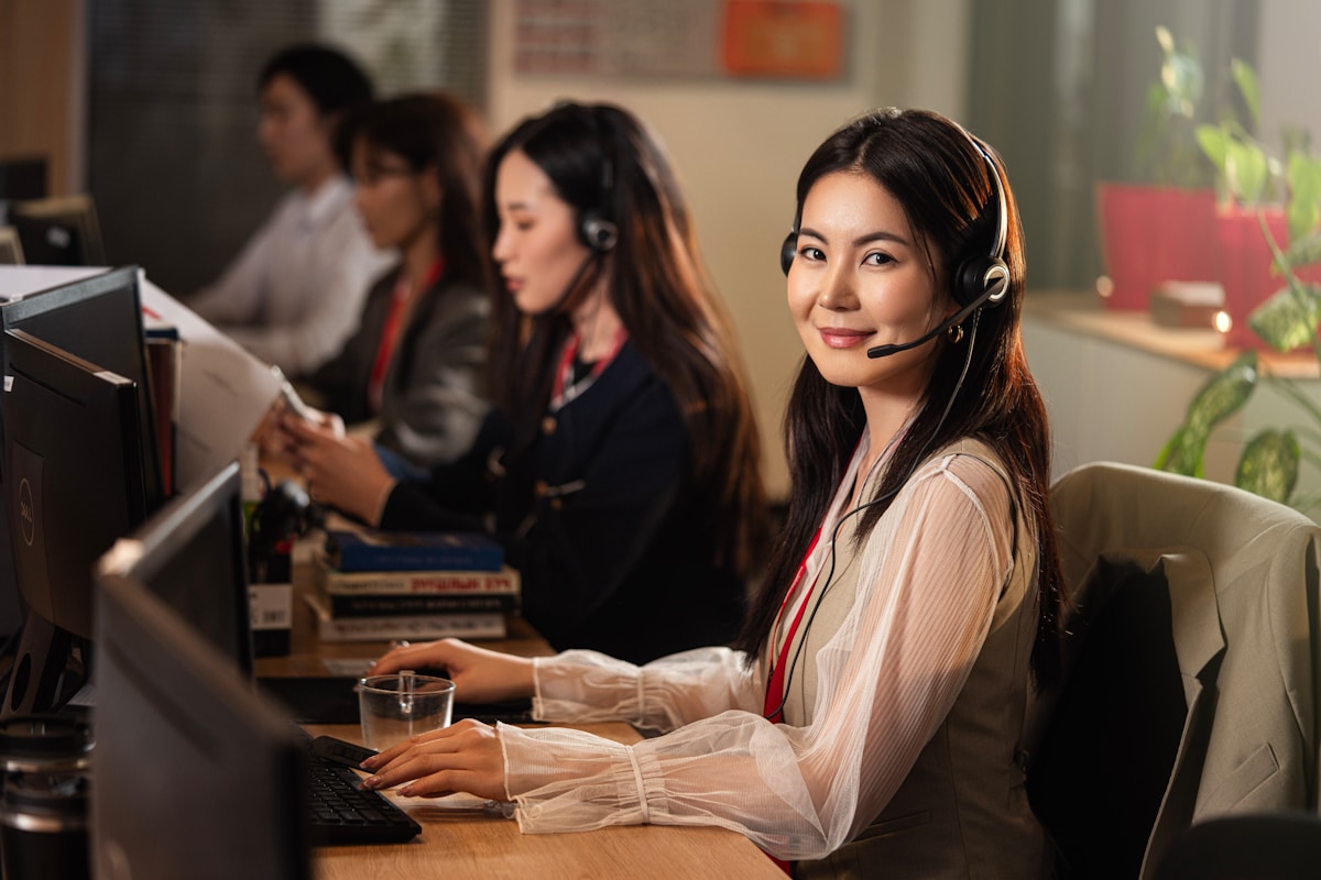 A smiling customer service representative wearing a headset at a support desk