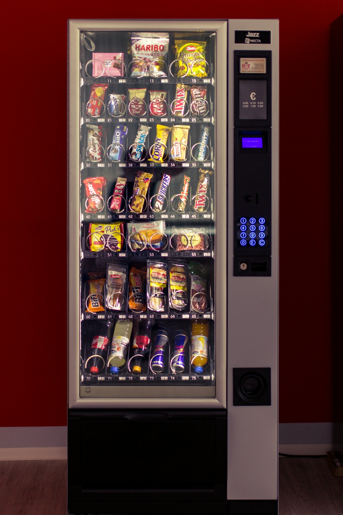 A brightly lit vending machine stocked with snacks and drinks against a deep red wall
