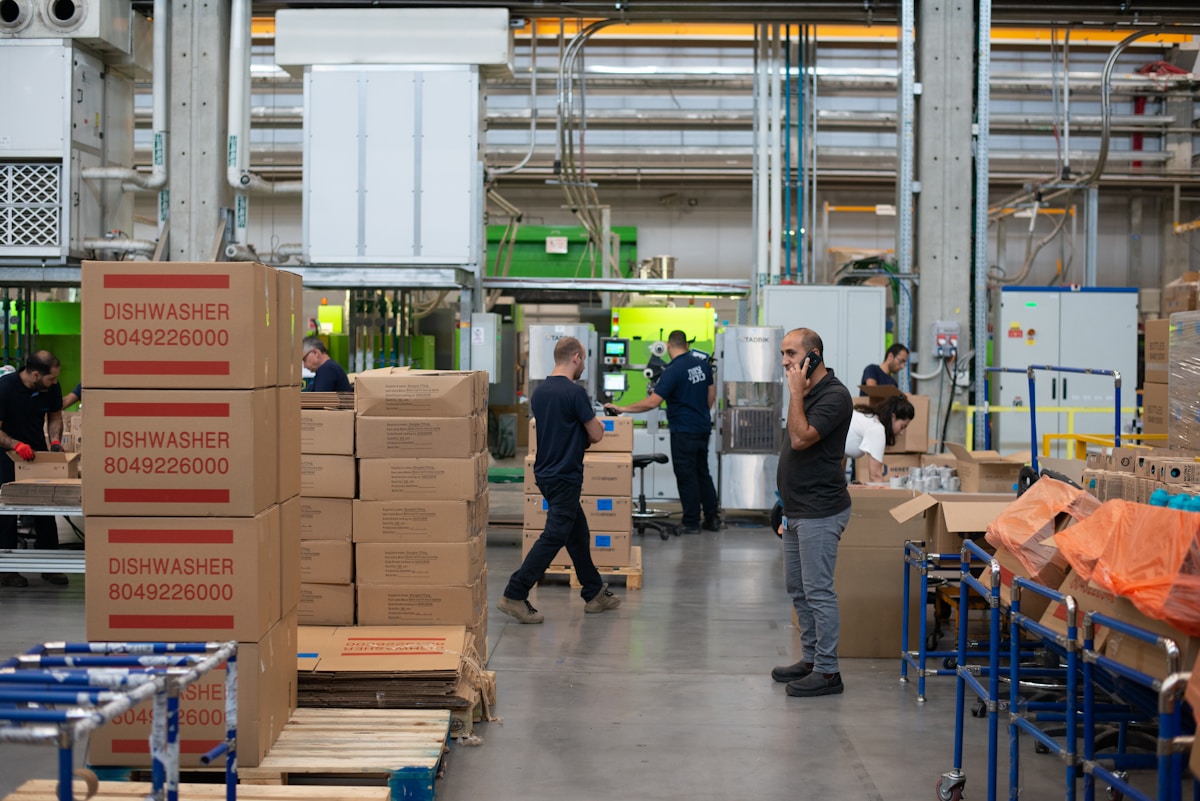 Workers on a manufacturing floor beside stacked boxes and machinery