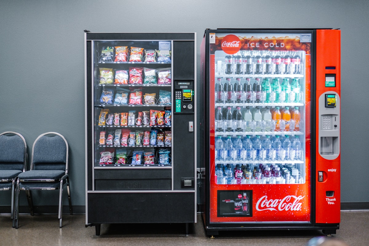 A snack vending machine and a red beverage vending machine installed side by side in a workplace break room